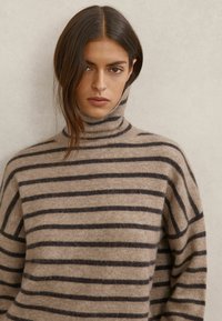 Sweter z golfem w paski w kolorze beżowym i ciemnobrązowym. Miękka tekstura o luźnym kroju, z pionowymi paskami i wysokim kołnierzem.