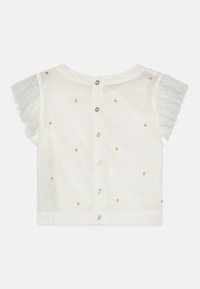 Hvit kortermet bluse med rynkede detaljer, prydet med gull- og sølvdekorative prikker og med knappelukking bak.