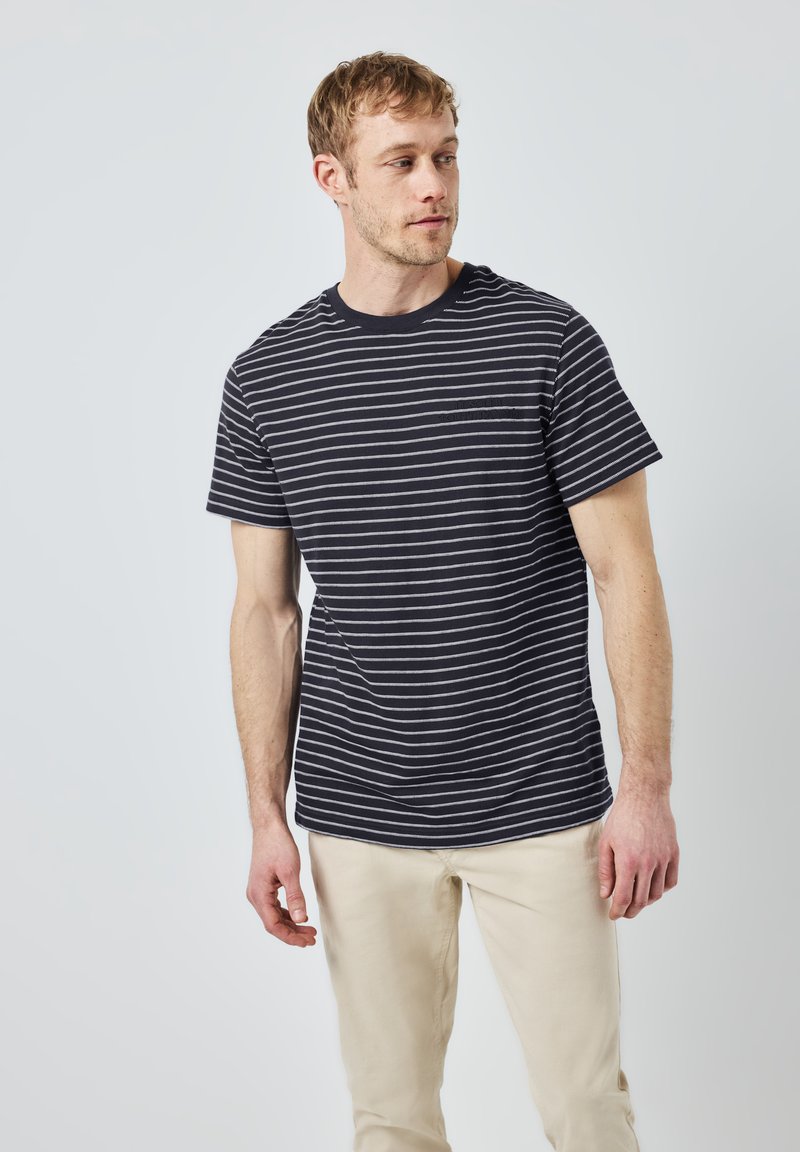 Námořnické modro-bílé pruhované tričko z bavlny s kulatým výstřihem a krátkými rukávy, nošené s světle béžovými kalhotami.