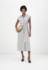 Rochie cu dungi, cu nasturi, albă și neagră, cu mâneci scurte, cu un cordon la talie și lungime midi. Este însoțită de o poșetă bej și tocuri negre.