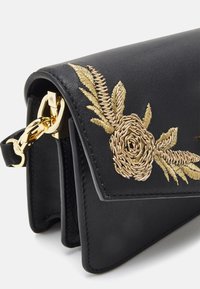 Black leather bag featuring gold floral embroidery and a chain accent. The design includes a flap closure and textured detailing.
