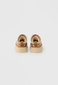 Paire de chaussures à enfiler imprimé léopard marron avec semelles épaisses beige et doublure en polaire douce, vues de dos sur un fond uni.