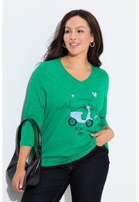 Maglietta verde a scollo a V con maniche a tre quarti, con grafica di uno scooter e scritta "Ciao Bella Roma 1983". Borsa nera con forma curva.