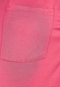 Růžová látka s hladkým povrchem a náprsní kapsou. Švy jsou viditelné podél okrajů kapsy, hladce začleněné do materiálu.