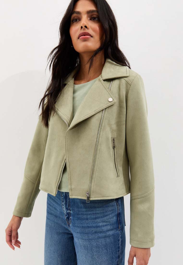 Woman wearing sage green suede biker jacket with zippered pockets and collar, paired with light green top and blue jeans.