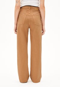 Jean en coton à jambes larges de couleur marron, avec une texture lisse, présentant une taille haute et quatre poches à l'arrière.