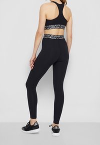 Schwarzes Sportset bestehend aus einem Racerback-Sport-BH mit Logo-Band und hochgeschnittenen Leggings; glatte Textur, figurbetonte Silhouette, minimalistisches Design.