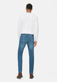 Herenoutfit bestaande uit een effen wit overhemd met lange mouwen en middelblauwe jeans met twee achterzakken, gedragen met bruine schoenen.