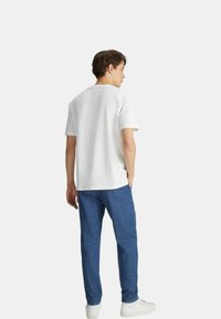 Maglietta bianca a collo rotondo con maniche corte, abbinata a pantaloni in denim blu e sneaker bianche. Texture liscia, design semplice, senza motivi visibili.