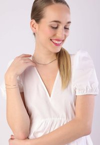 Silver bracelet and necklace; the necklace is a thin chain, while the bracelet features a simple design. Model wears a white puff-sleeve top.