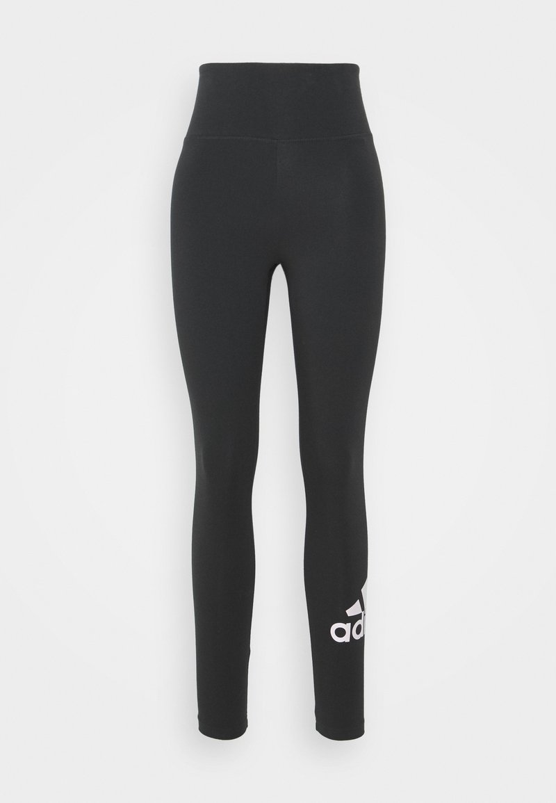 Černé legíny Adidas s vysokým pasem, přiléhavými nohavicemi a bílým logem Adidas na dolní části levé nohavice na jednobarevném pozadí.
