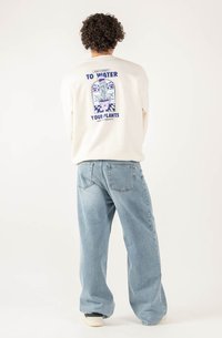 Felpa crema con design grafico sul retro raffigurante piante in un vaso e la scritta "Non dimenticare di annaffiare le tue piante." Abbinata a jeans blu chiaro.