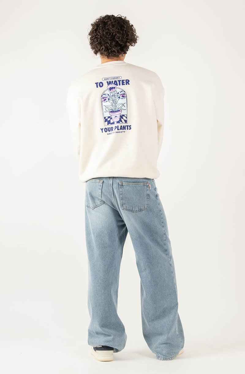 Felpa crema con design grafico sul retro raffigurante piante in un vaso e la scritta "Non dimenticare di annaffiare le tue piante." Abbinata a jeans blu chiaro.