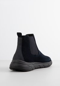 Stivaletti neri in suede con pannelli laterali elasticizzati, punta arrotondata e suola in gomma texturizzata. Progettati per comfort e stabilità.