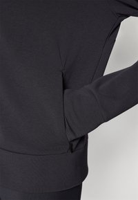 Dark gray sweatshirt with a fitted design, featuring a side pocket, ribbed cuffs, and a smooth texture. Minimalist stitching detail present.