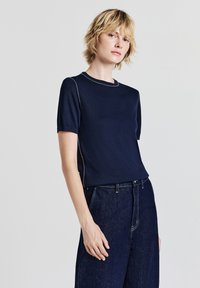 Maglietta a maniche corte blu navy realizzata in tessuto morbido, con scollatura rotonda e cuciture bianche a contrasto lungo le cuciture.
