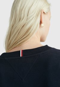 Felpa navy con collo a coste, caratterizzata da una piccola striscia rossa, bianca e blu. Tessuto morbido, design minimalista.