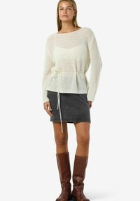 Maglione leggero color crema in maglia con vita con coulisse, abbinato a una gonna di jeans scuro e stivali marroni al ginocchio.