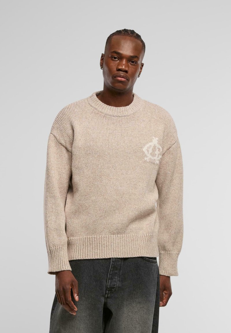 Beige gestrickter Pullover mit Rundhalsausschnitt, gerippten Bündchen und Saum, der ein dezentes cremefarbenes Logo im linken Brustbereich aufweist.