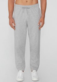 Gray cotton sweatpants with elastic cuffs and a drawstring waistband, paired with white sneakers. Soft texture, relaxed fit.