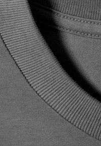 Γκρι φούτερ με ριμπ λαιμόκοψη και υφή υφάσματος, με επίπεδες ραφές και απαλό φινίρισμα, που αναδεικνύει τις λεπτομέρειες του σχεδιασμού του ενδύματος.