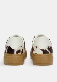 Tenisi cu un model brun și alb, cu accente din piele netedă și talpi din cauciuc texturat. Dispun de coliere captusite și un design low-top.