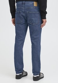 Jeans hlače iz temno modrega denima z ravnim krojem nogavic, vidnimi šivi, dvema zadnjima žepoma in rjavim etiketo na pasu.