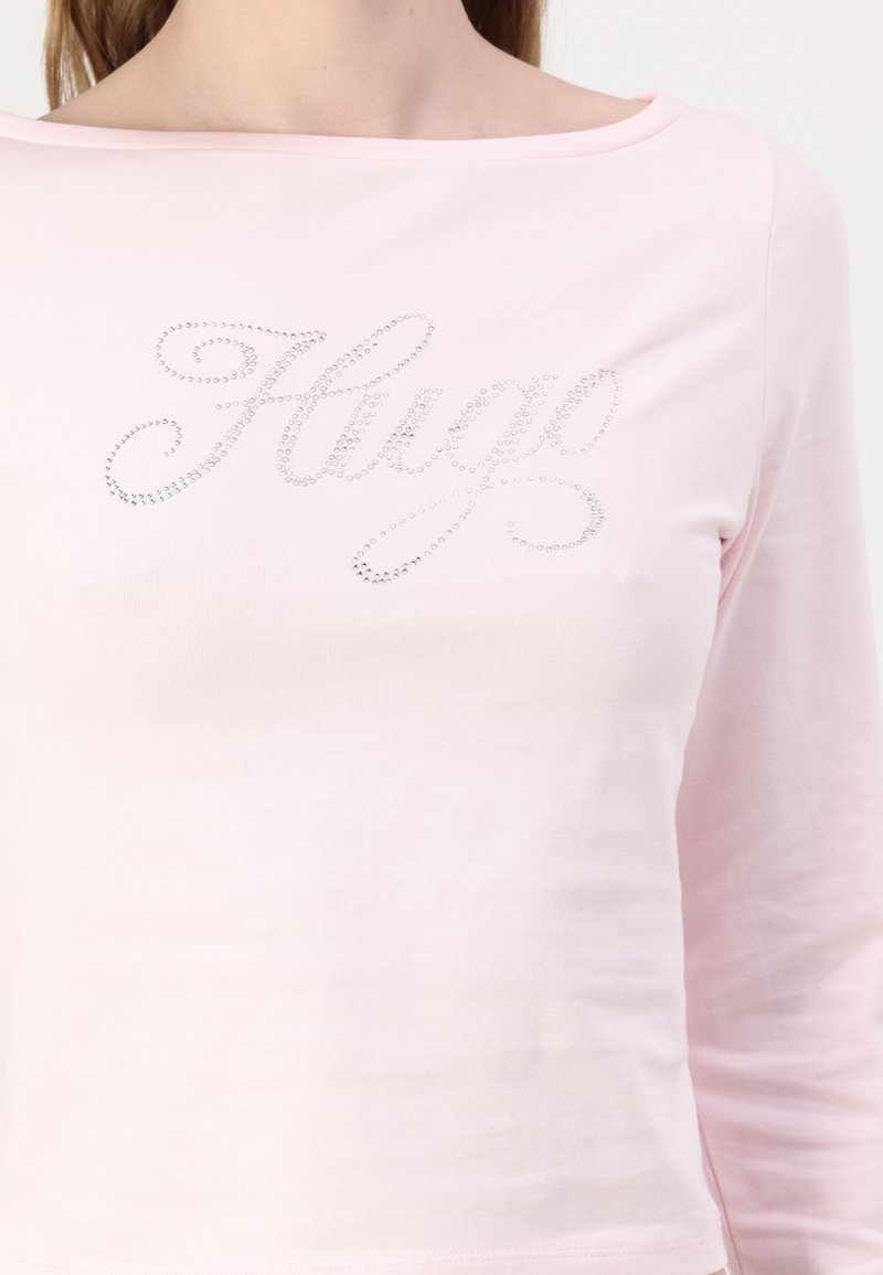 Ljusrosa långärmad tröja med båtutskärning som har glänsande rhinestones som formar ordet "Hugo" över bröstet. Mjuk, slät tyg.