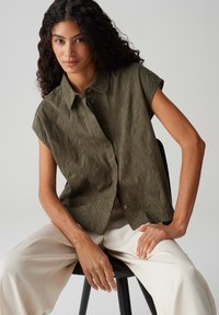 Groene korteknip shirt met een gestructureerd bladenpatroon, voorzien van een knoopsluiting aan de voorkant en een relaxed fit, gecombineerd met crème wijd-uitlopende broek.