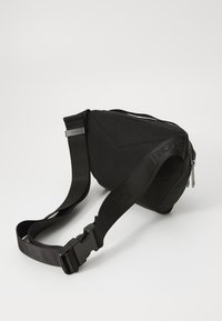 Borsa a tracolla in tessuto nero con texture a rete, cinturino regolabile e scomparto principale con zip. Presenta un dettaglio del logo laterale e chiusura a fibbia.