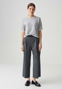 Grijze kortek MMS-shirt met witte rand, gecombineerd met hoge taille, wijde streepbroek en zwarte instappers op een neutrale achtergrond.