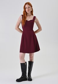 Bordeaux mouwloze jurk met een sweetheart-halslijn en een uitlopende rok. Draagt het met zwarte laarzen tot de knie met gouden ritsen.