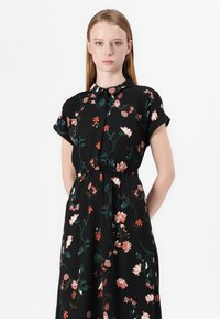 Robe noire à fleurs avec des manches courtes, un col et une taille élastique. Présente des fleurs roses et vertes sur un fond sombre.