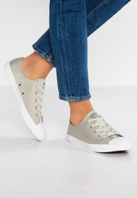 Baskets en toile gris clair avec semelles en caoutchouc blanc, dotées d'œillets et de lacets dorés, et d'un design à bout rond.