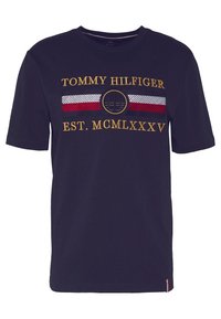 Námořnická modrá bavlněná tričko s krátkým rukávem, zdobené žlutou výšivkou "TOMMY HILFIGER" a pruhovaným designem v červené, bílé a modré barvě.