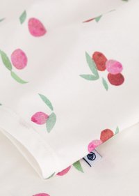 Tessuto in cotone bianco con un motivo ripetuto di cerchi rosa e rossi accompagnati da foglie verdi. Bordo ripiegato visibile con una piccola etichetta di tessuto.