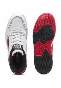 Sneakers Puma z białą skórzaną cholewką, czarnymi i czerwonymi akcentami, płaskimi sznurówkami oraz fakturowaną czarną i czerwoną gumową podeszwą.
