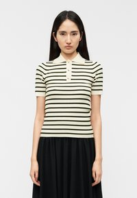 Ριγέ πόλο μπλουζάκι με κοντά μανίκια σε εκρού και σκούρο πράσινο, με ριμπ υφή, διαθέτει γιακά και τρία διακοσμητικά κουμπιά.