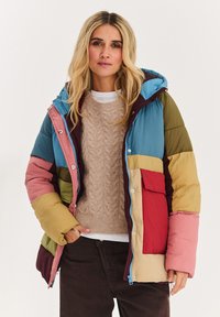 Prošívaná bunda s kombinací modrých, zelených, růžových a vínových panelů, se zipem, kapucí a červenou přední kapsou.