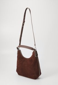 Braune Wildleder-Schultertasche mit einem braunen Ledertrageriemen, gekennzeichnet durch eine gebogene Oberseite, einen Reißverschluss und eine glatte Textur. Weiche, unstrukturierte Form.