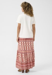 Un tricou alb cu mânecă scurtă, asortat cu o fustă maxi roșie, cu un model tipar și un design cu volane, având motive florale subtile. Sandale cu toc bloc maro.
