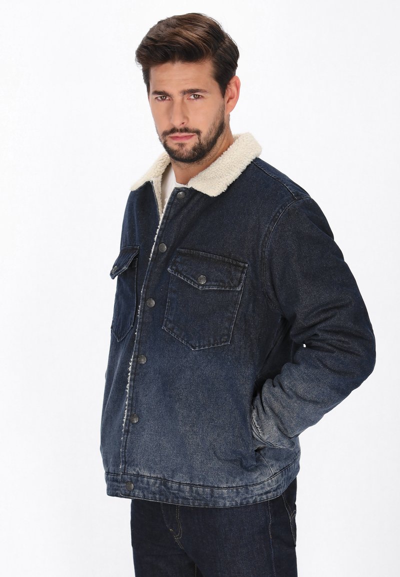 Sötét kék farmerdzseki plüss, tört fehér szegéllyel, két mellzsebbe és gombos zárással. Tartós anyagból készült, laza fazonnal.