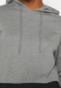 Gray cropped hoodie made of soft fabric with a drawstring hood, featuring silver metal tips on the drawstrings and a relaxed fit.