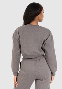 Grijze cropped sweatshirt van zachte stof met verlaagde schouders en geribbelde zoom, gecombineerd met bijpassende broeken in een vergelijkbare textuur en kleur.