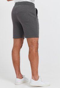 Gray athletic shorts with a snug elastic waistband, side pockets, and a back patch pocket. Worn with white sneakers.