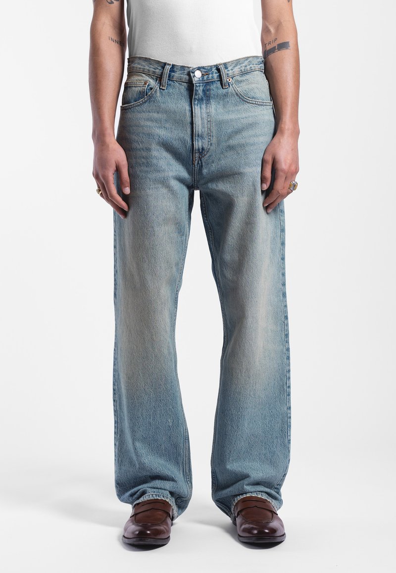 Lichtblauwe, high-waisted jeans van denim, met een rechte pijp en vervaagde textuur. Draagt met bruine schoenen en een witte tanktop.