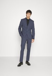 Navy blue checked suit with slim fit blazer and trousers. Paired with a black shirt and black dress shoes, showcasing tailored design and sleek lines.