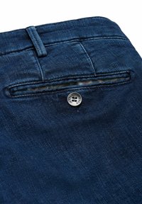 Un pantalon en denim bleu foncé présente une poche arrière avec une fermeture à bouton et une surface de tissu texturée. Il y a peu de détails de couture visibles.