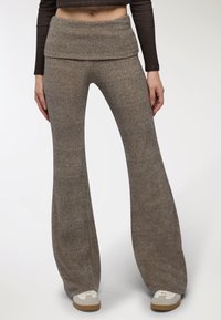 Szare rozszerzane spodnie wykonane z miękkiego materiału, z szerokim paskiem na brzuchu, gładką teksturą i luźnym krojem sięgającym do kostek.