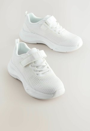 Valged spordijalatsid, millel on tekstuuriga võrkkangas, pitsid ja Velcro rihmad, pehmendatud krae ning paks kummist tall. 